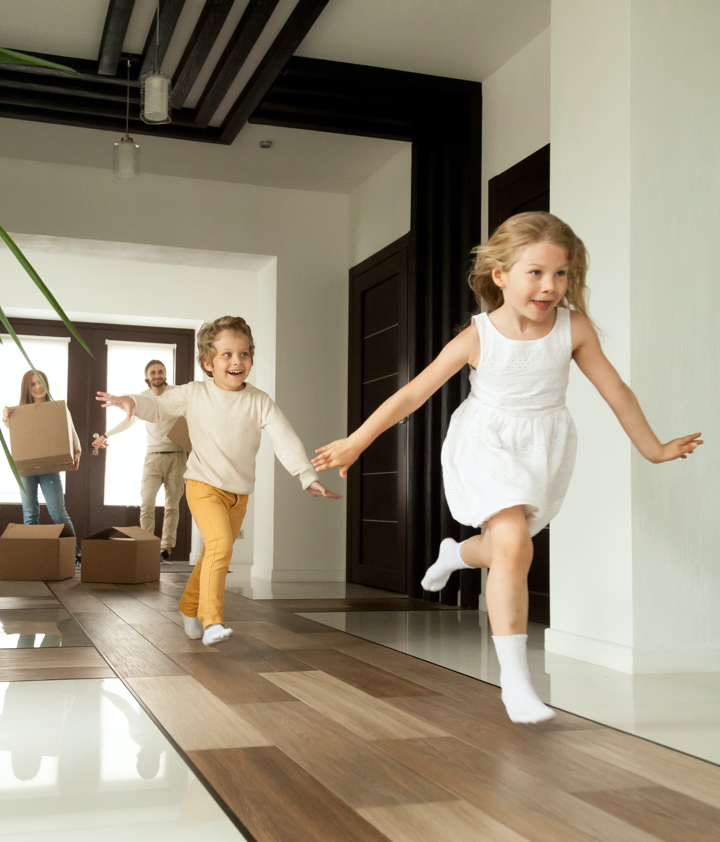 Excited children running into big modern house with parents in the background