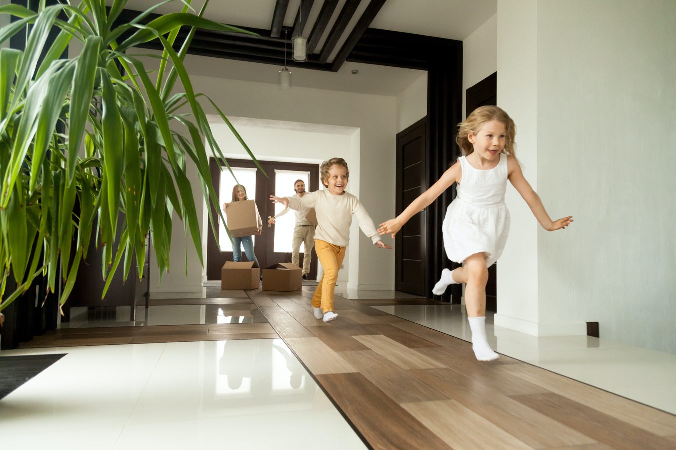 Excited children running into big modern house with parents in the background (large image)